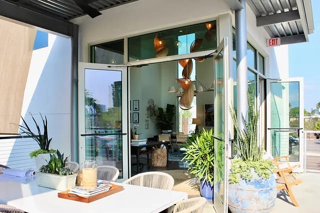 Patio with white table, chairs, potted plants, and sliding glass doors leading to an interior.