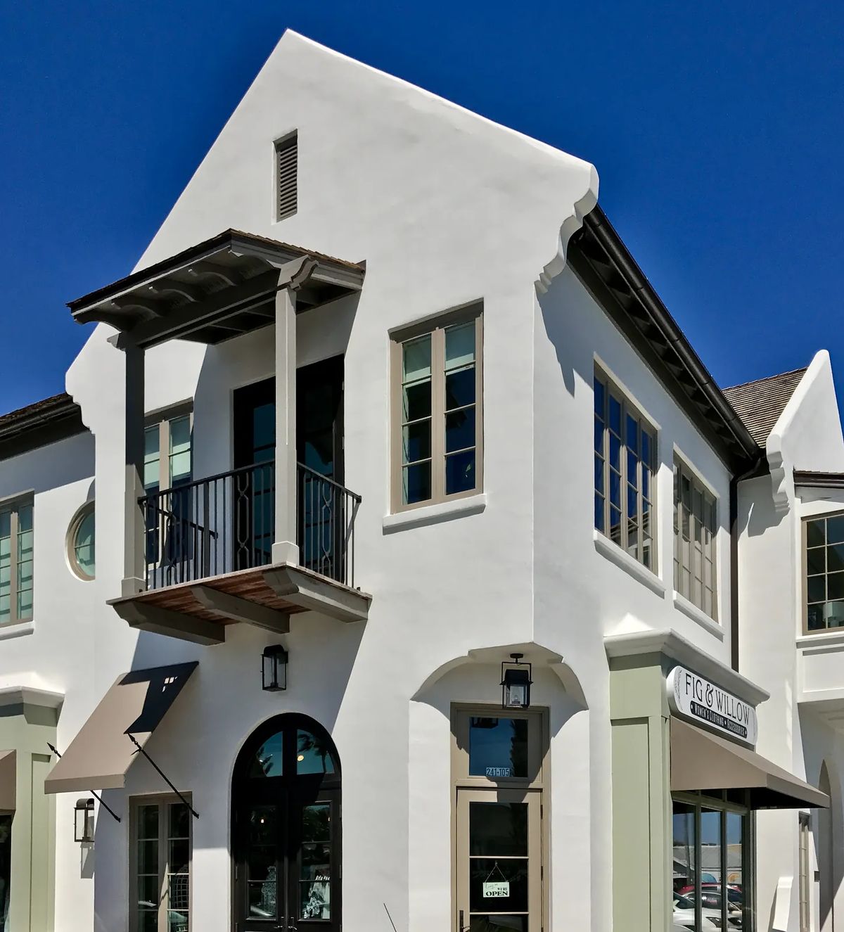 Exterior front view of a building with white stucco, large windows, balcony, and decorative eaves.