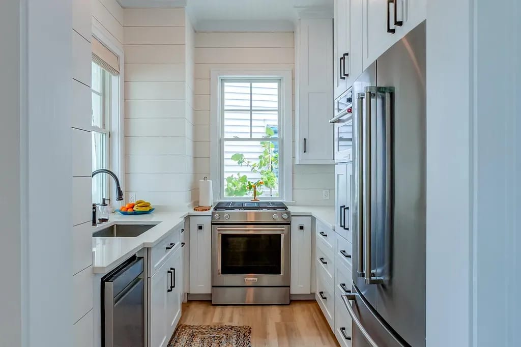Kitchen with white cabinetry, stainless steel appliances, large sink, and window with greenery.