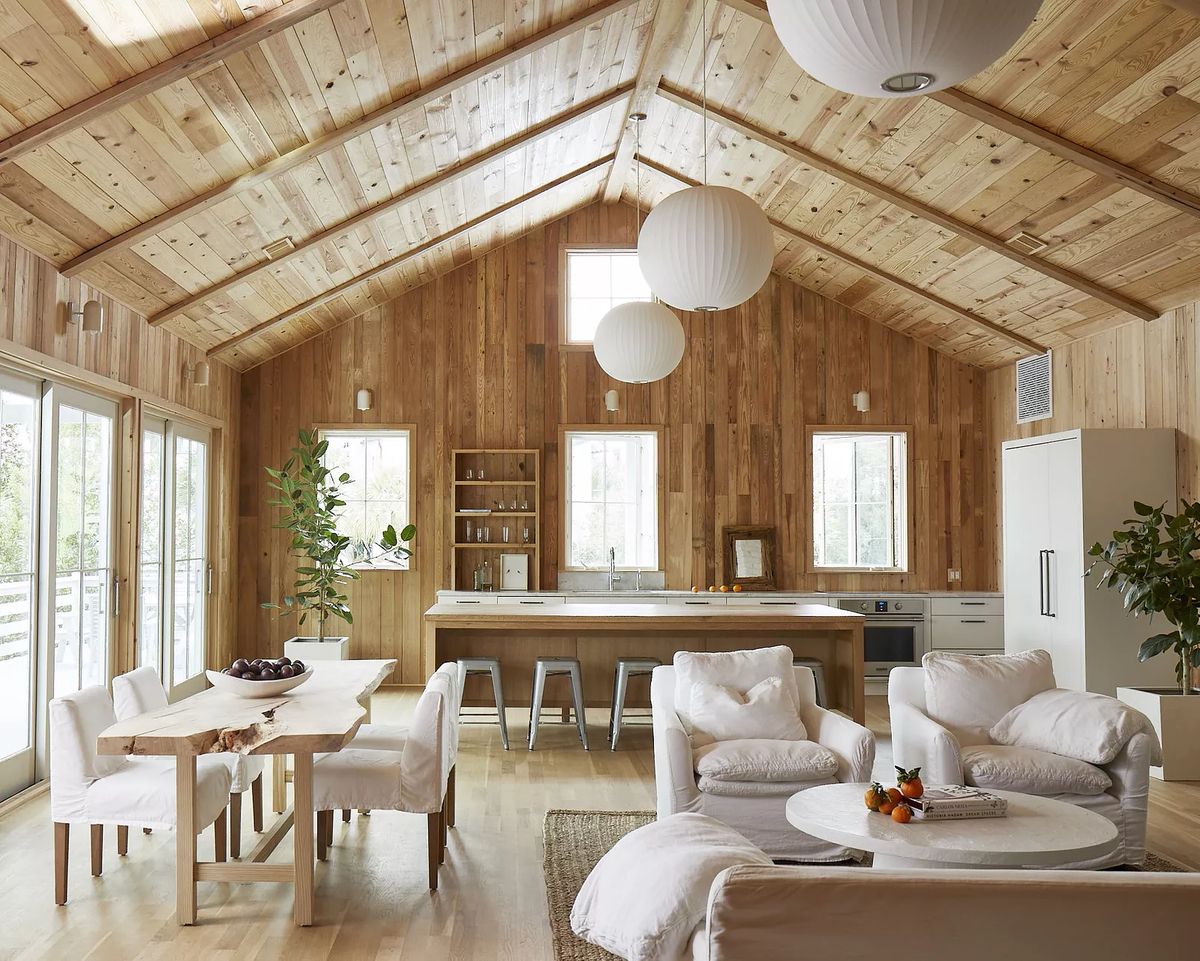 Living room with wood paneled walls, white sofa, coffee table, dining table, and large windows.