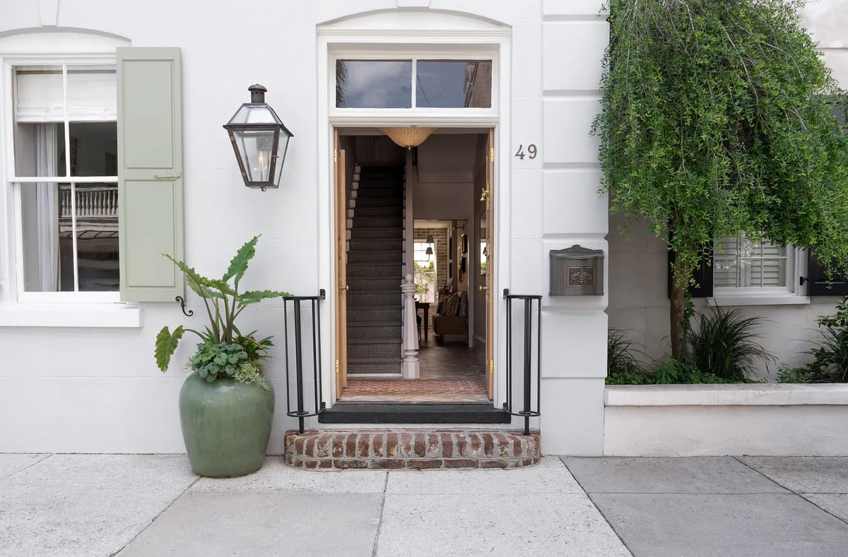 Exterior front view with white facade, green shutters, lantern, brick step, and ornamental planter.