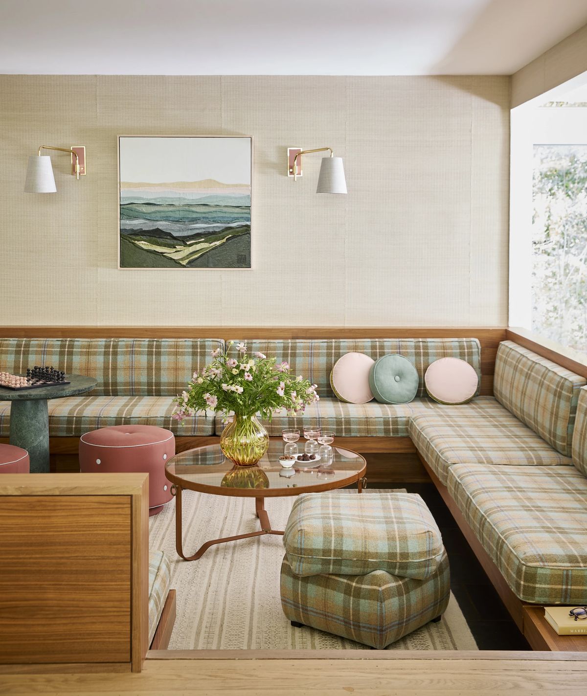 Living room with plaid sectional sofa, round glass coffee table, floral arrangement, and wall sconces.