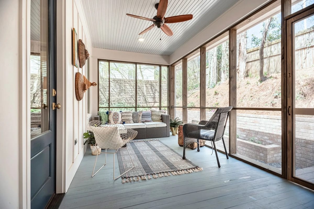 Screened porch with gray wicker seating, patterned rug, ceiling fan, and wooden walls.