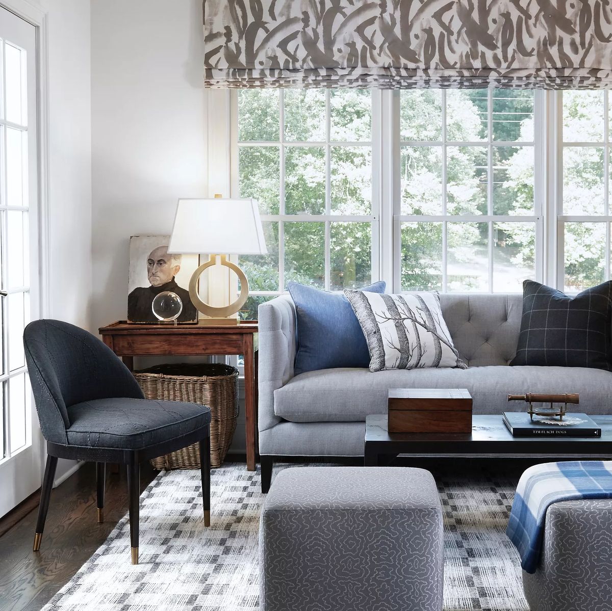 Living room with gray tufted sofa, black chair, wood side table, coffee table, and large area rug with natural light.