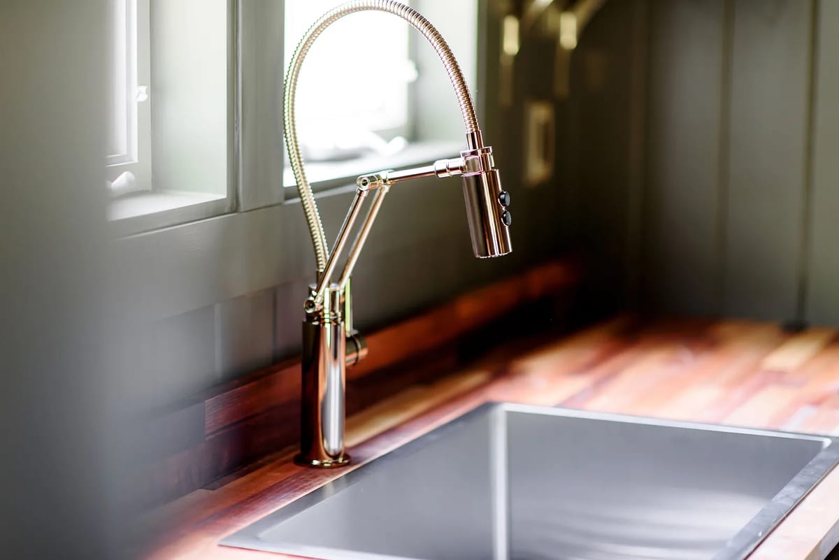 Kitchen sink area with modern faucet, stainless steel sink, and wooden countertop with natural light from windows.