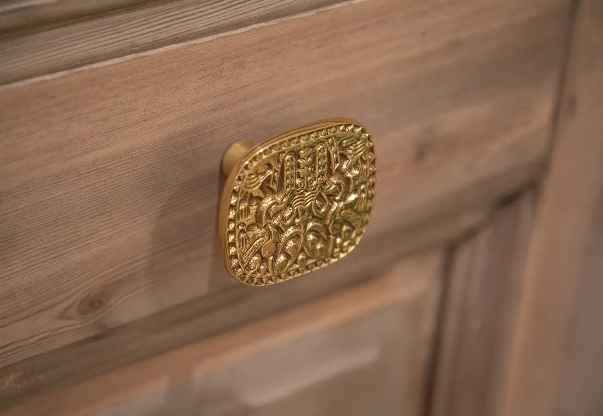 Close-up of textured wood with a gold decorative knob featuring intricate patterns.