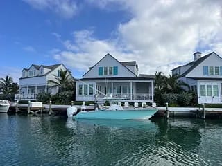 Waterfront view of two-story house with white siding, turquoise accents, and a docked turquoise boat.
