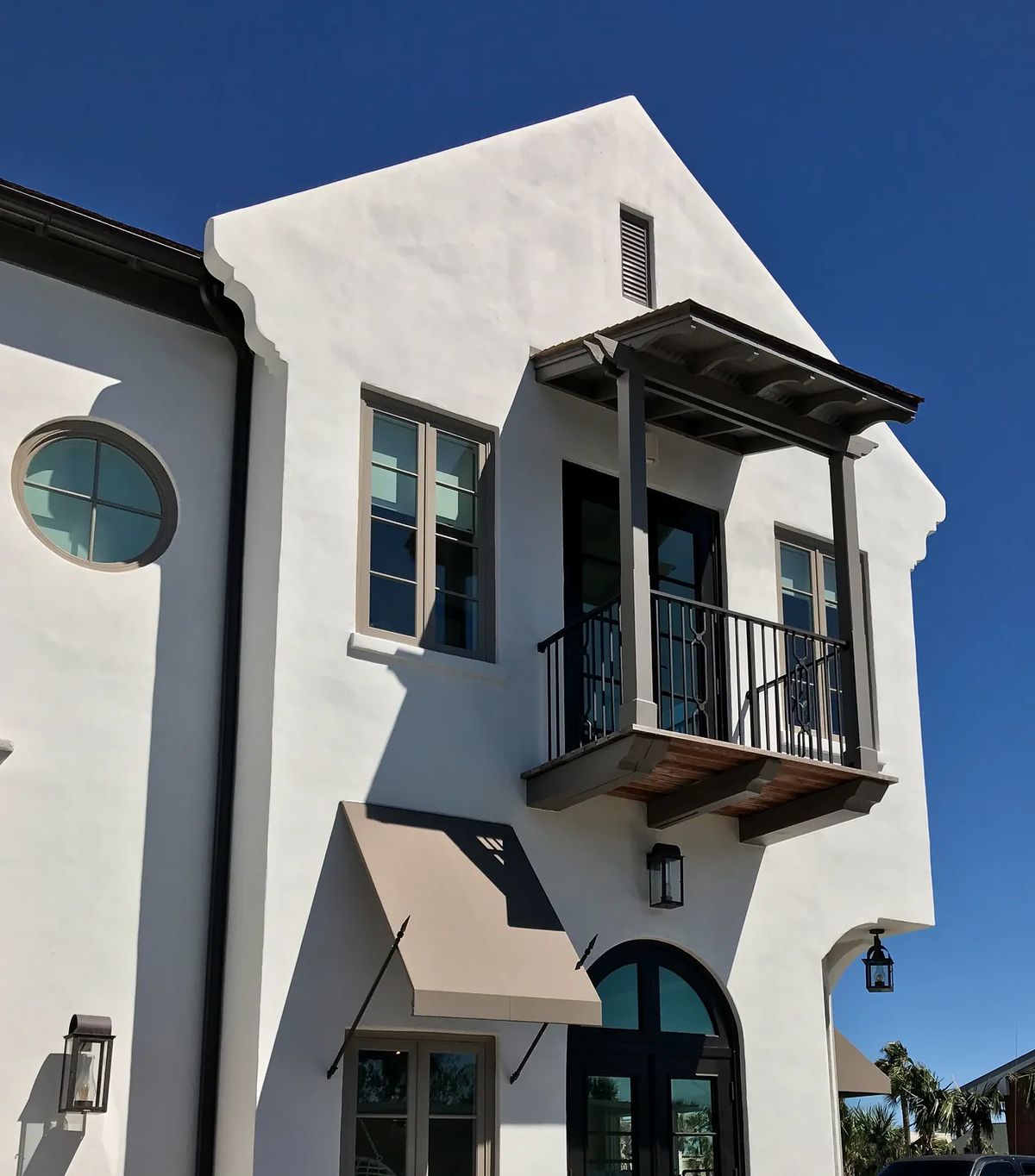 Exterior front view of a building with white stucco, balcony, large windows, and awning.