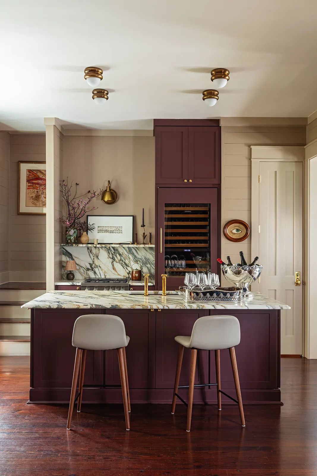 Kitchen with burgundy island, marble countertop, gray bar stools, wine cooler, and dark hardwood floor.