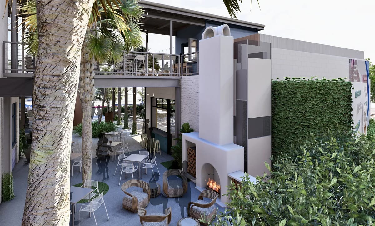 Outdoor patio with round tables, wicker lounge chairs, stone fireplace, and surrounding greenery.