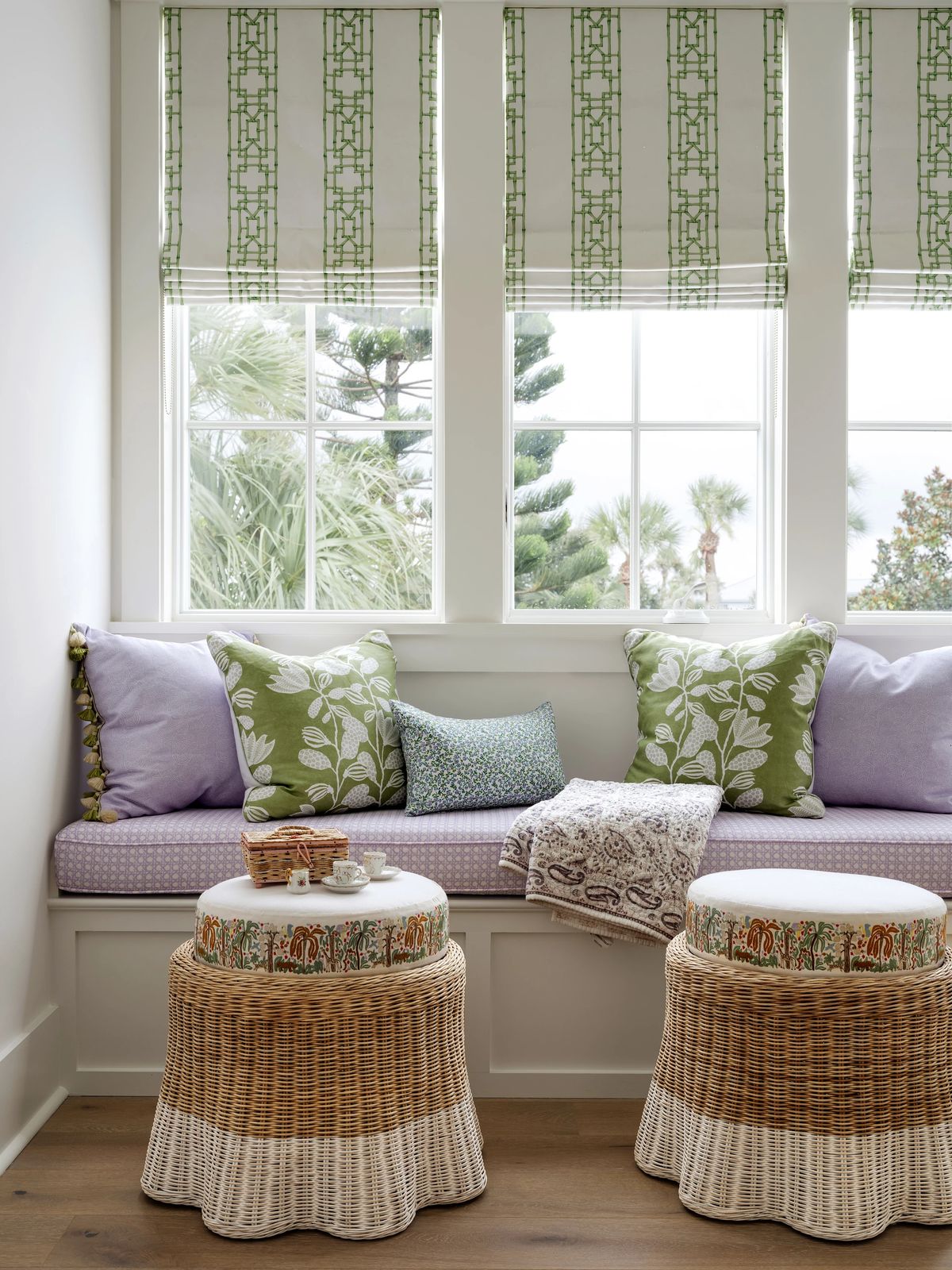 Seating area with bench, cushions, decorative pillows, wicker stools, and large windows with green shades.