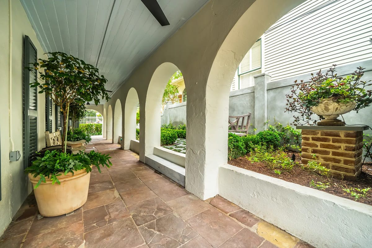 Patio with arched columns, stone floor, wooden benches, potted plants, and garden elements.