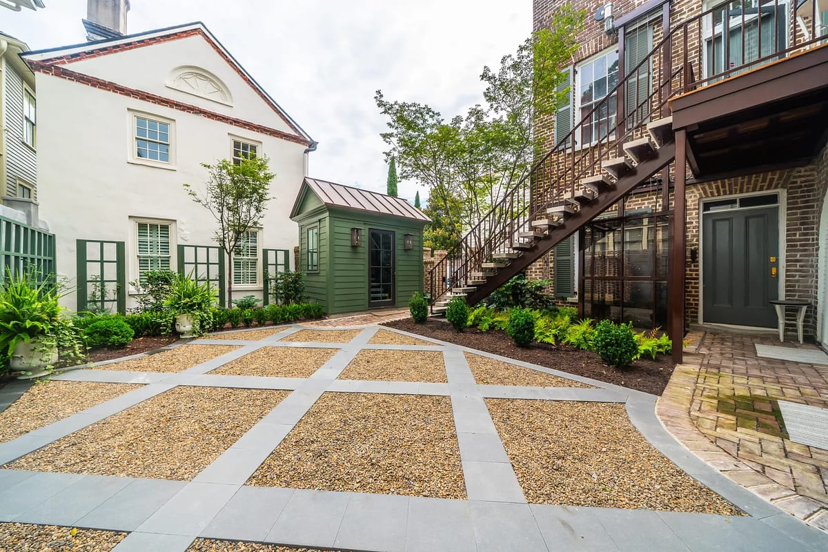 Outdoor garden with gravel pathway, potted plants, green shed, and surrounding shrubs.