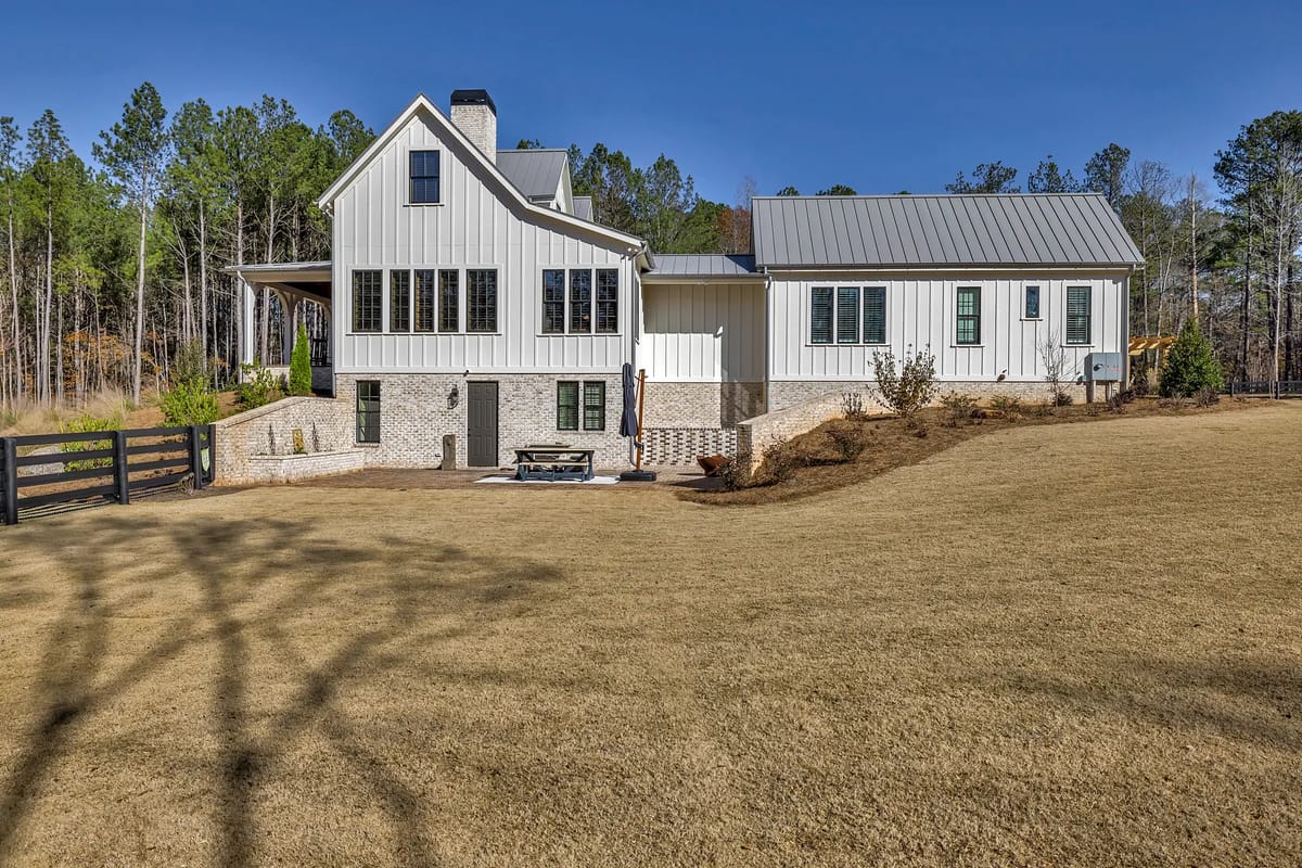 Exterior rear of house with white siding, gray metal roof, large windows, patio, and grassy lawn.