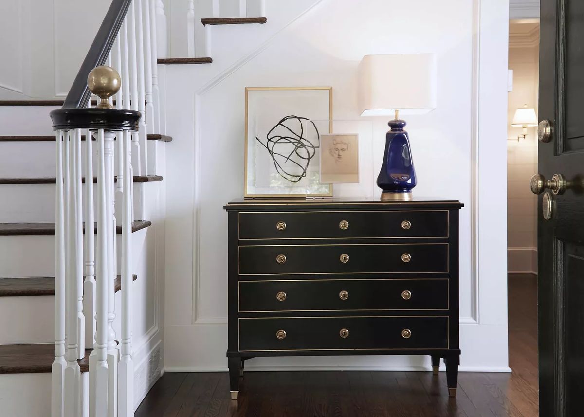 Foyer with black chest of drawers, abstract artwork, blue lamp, and wooden staircase with dark wood floor