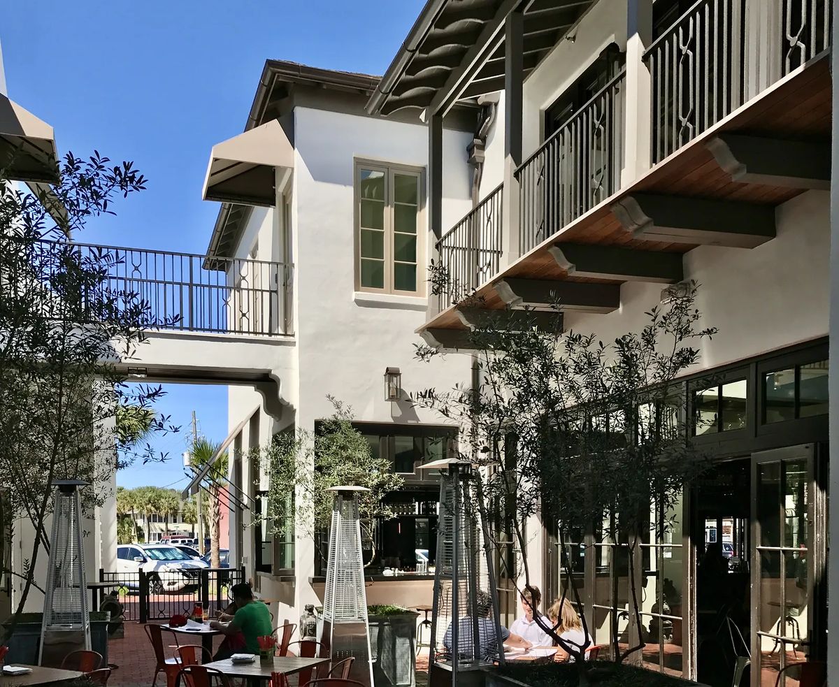 Patio area with metal tables, greenery, glass doors, and a wooden balcony.