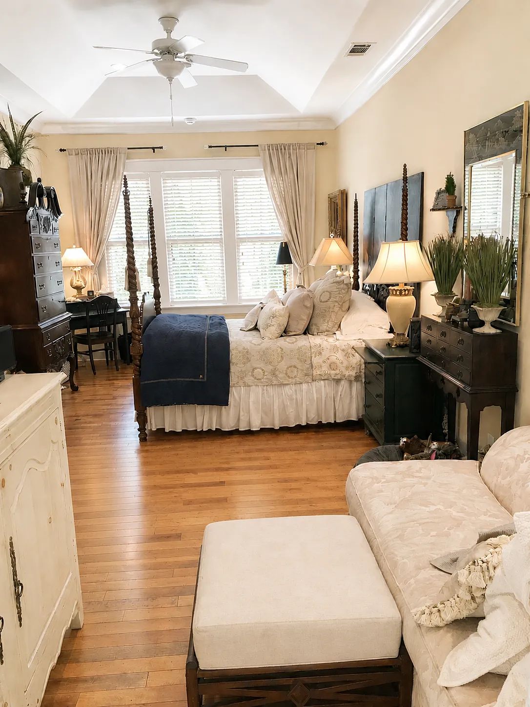 Bedroom with four-poster bed, nightstands, lamps, dresser, console table, sofa, and wooden flooring