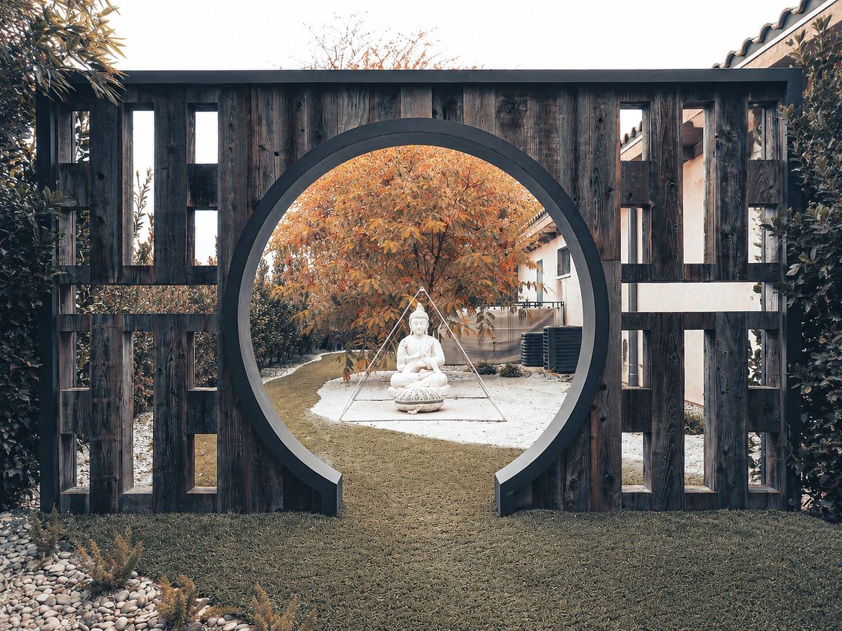 Garden with wooden archway, white statue, gravel path, and landscaped greenery.