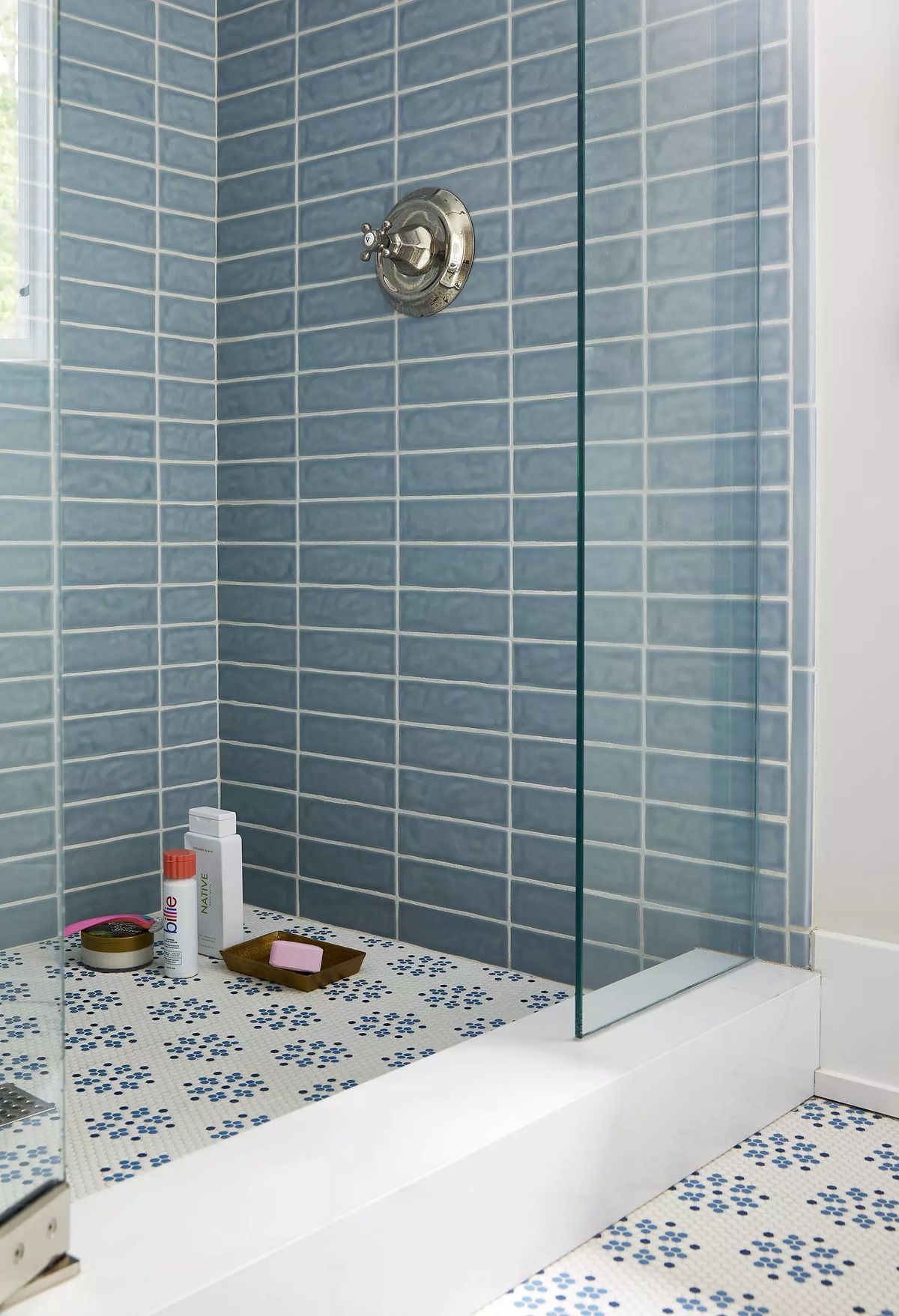 Bathroom with walk-in shower, blue tiled walls, glass door, and toiletries on wooden tray.