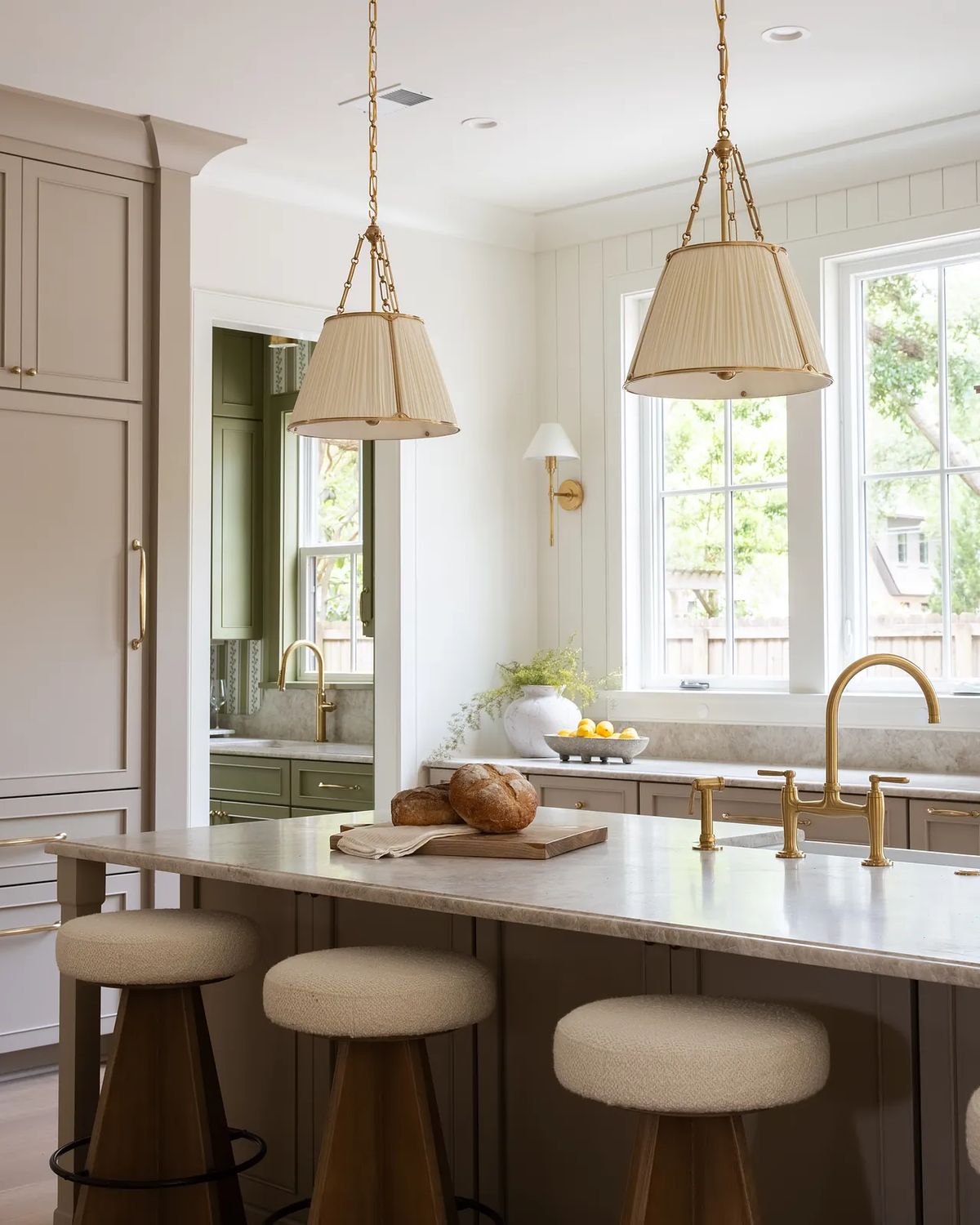 Kitchen with central island, three stools, light countertop, gray cabinets, and large windows.