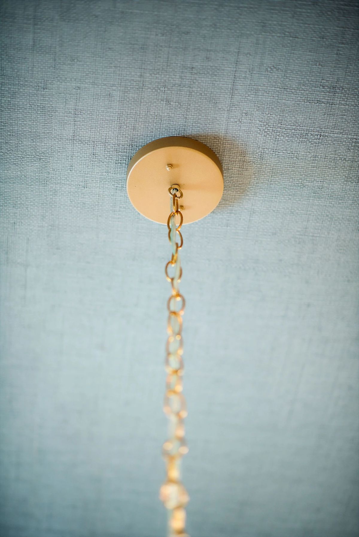 Ceiling fixture attachment with gold canopy and chain on a light blue surface.