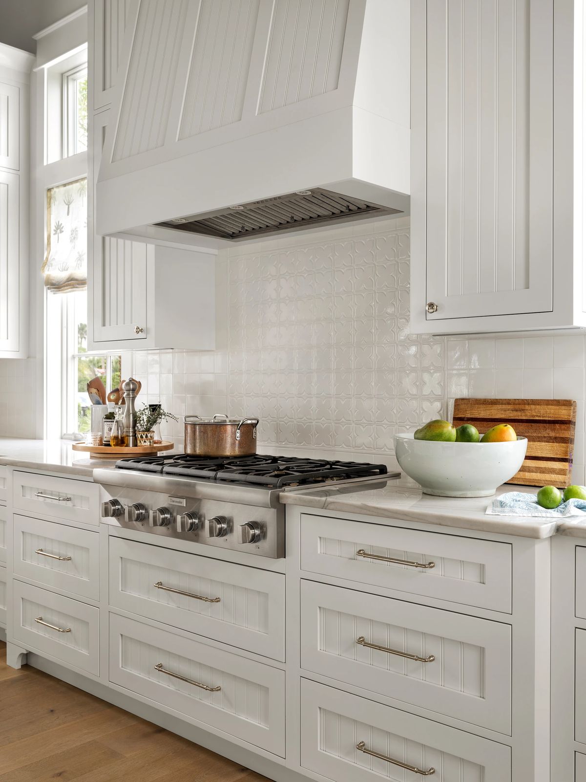 Kitchen with stainless steel stove, white cabinets, countertop, backsplash, bowl of fruit, and cutting board.