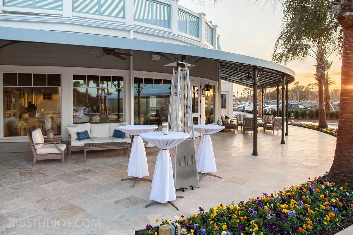 Outdoor patio with covered lounge area, tall tables, heater, and colorful potted flowers.