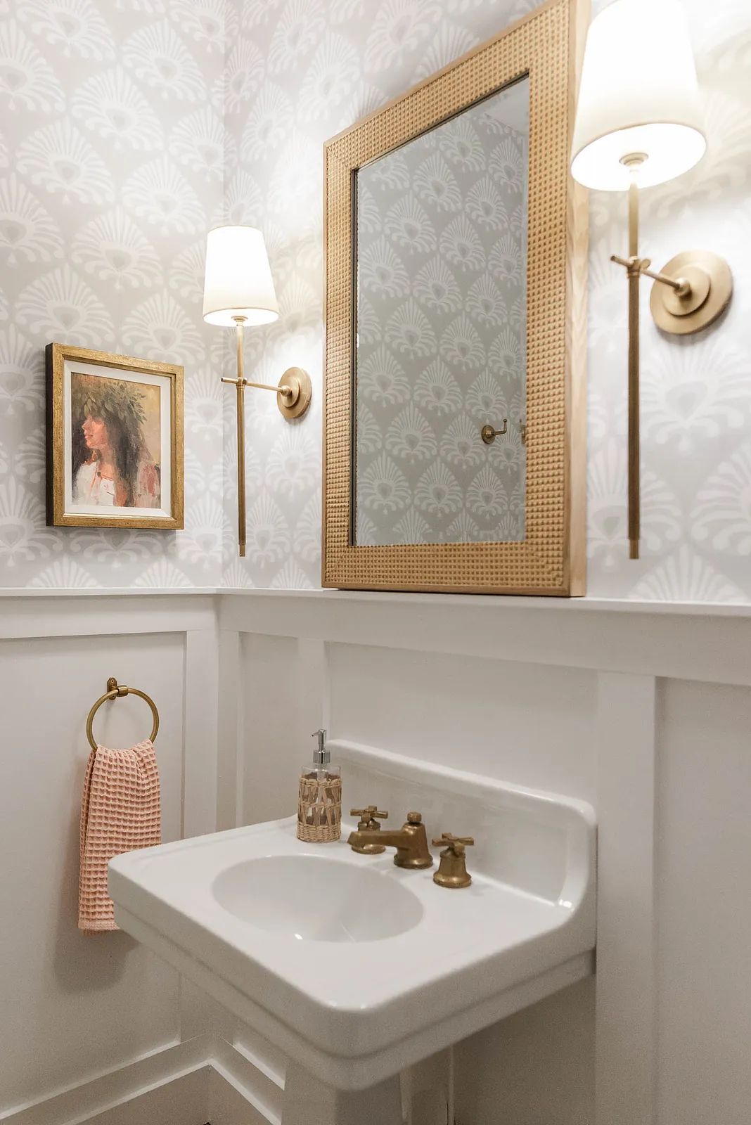 Powder room with wall-mounted sink, faucet, mirror, towel ring, sconces, patterned walls, and white wainscoting