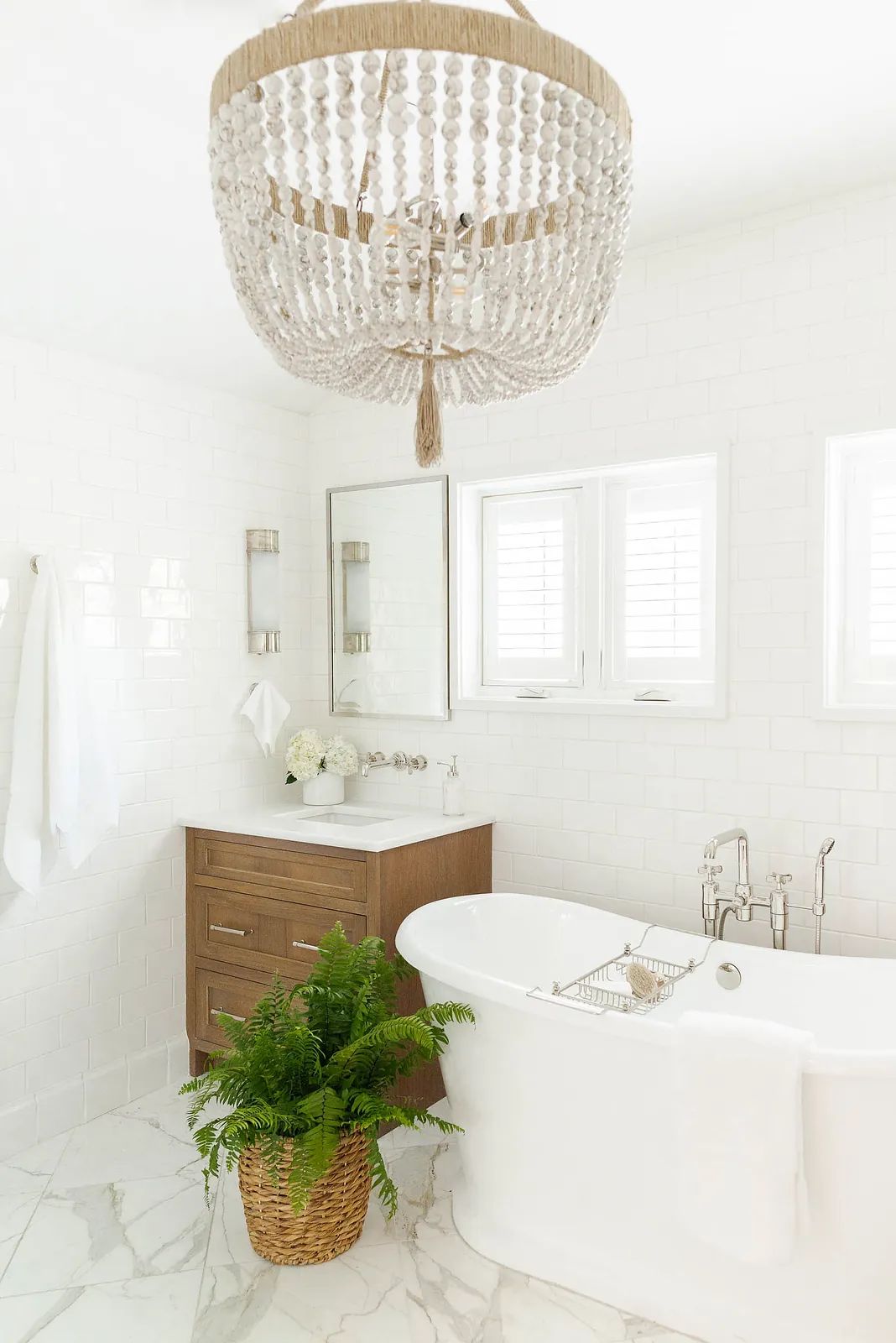 Bathroom with freestanding white bathtub, wood vanity, large mirror, and potted fern.