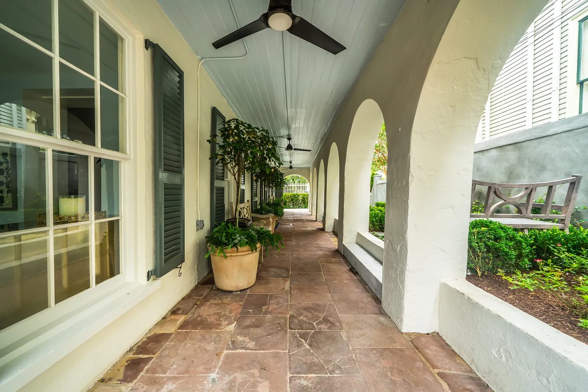 Hallway with stone floor, arches, potted plants, and ceiling fans.
