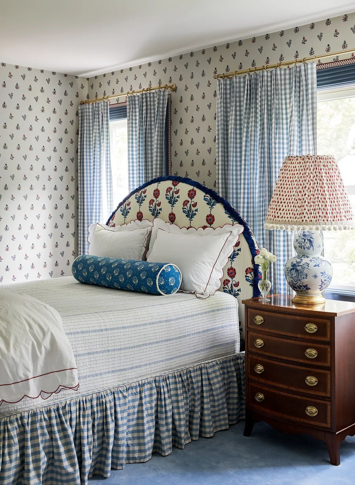 Bedroom with floral headboard, blue and white quilt, nightstand, and patterned wallpaper.