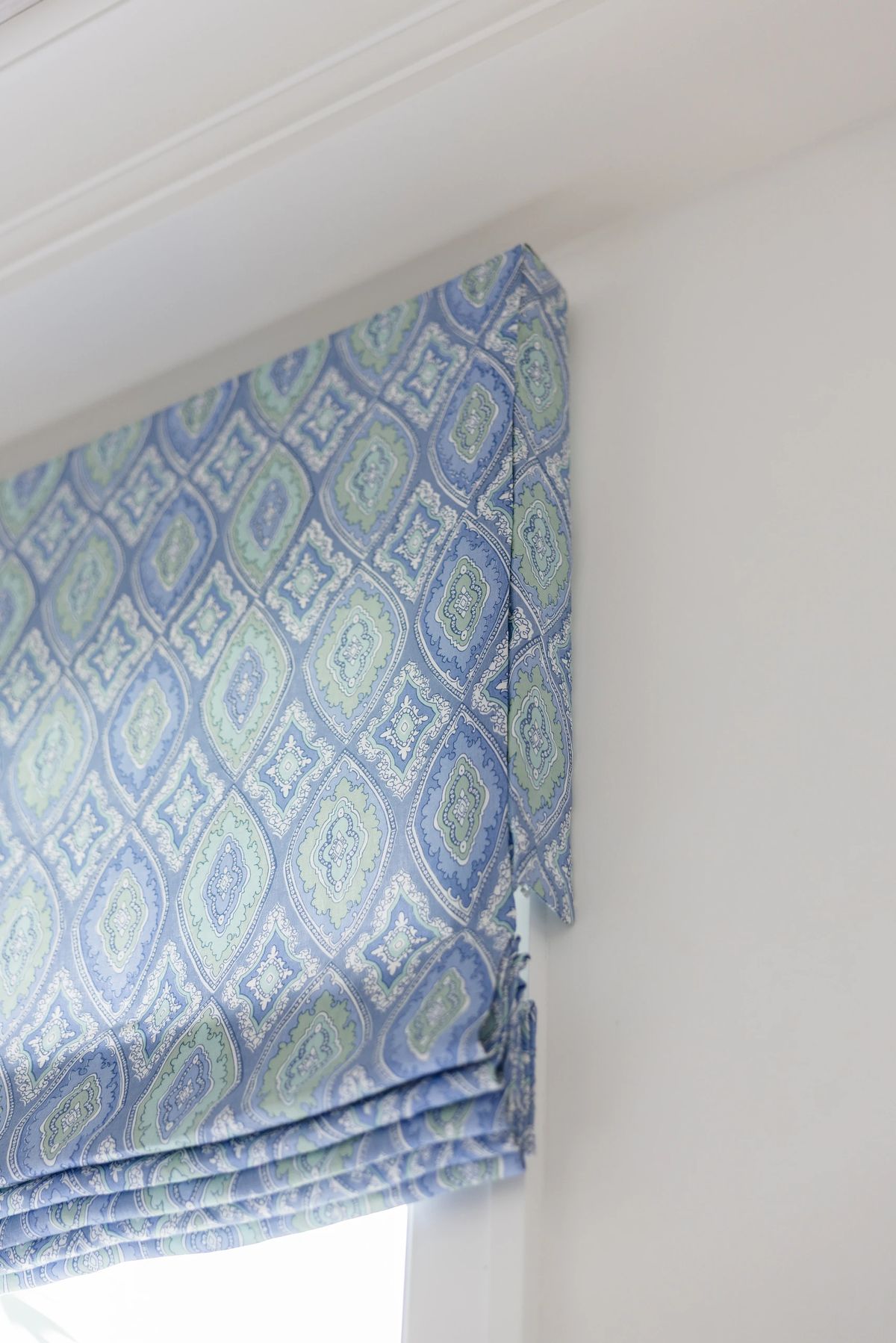 Window with blue and green patterned fabric shades and white wall.