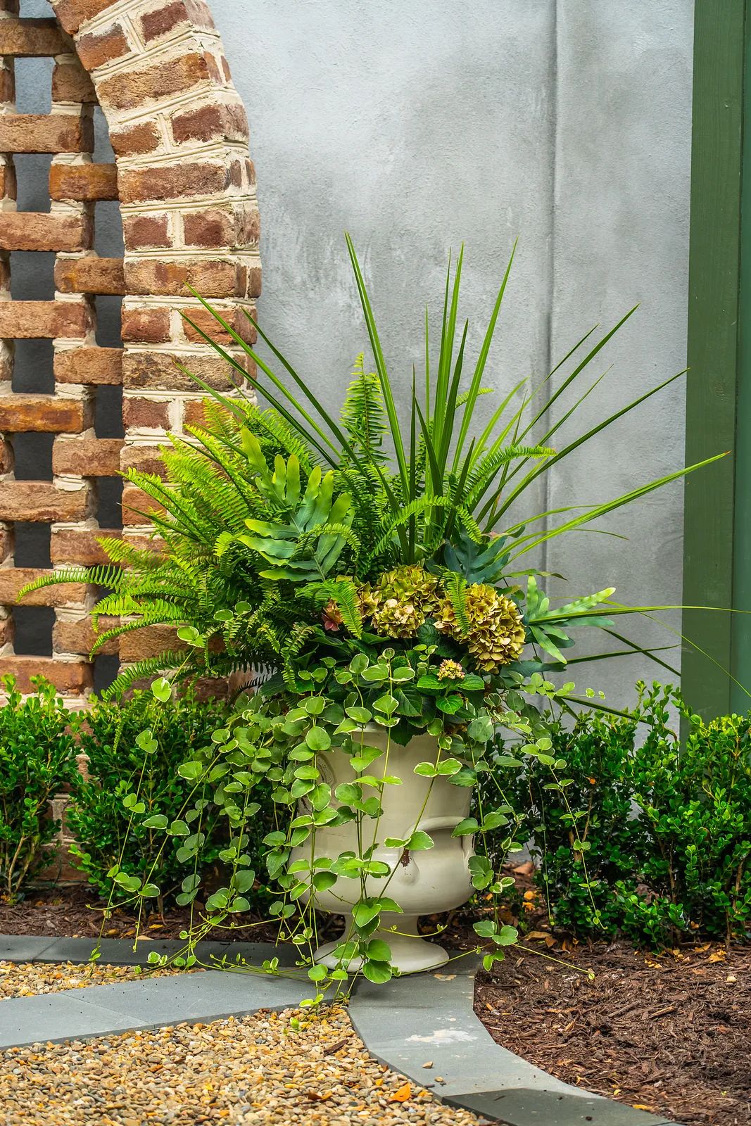 Garden with decorative plant arrangement in pot, brick wall, and trimmed boxwood shrubs.
