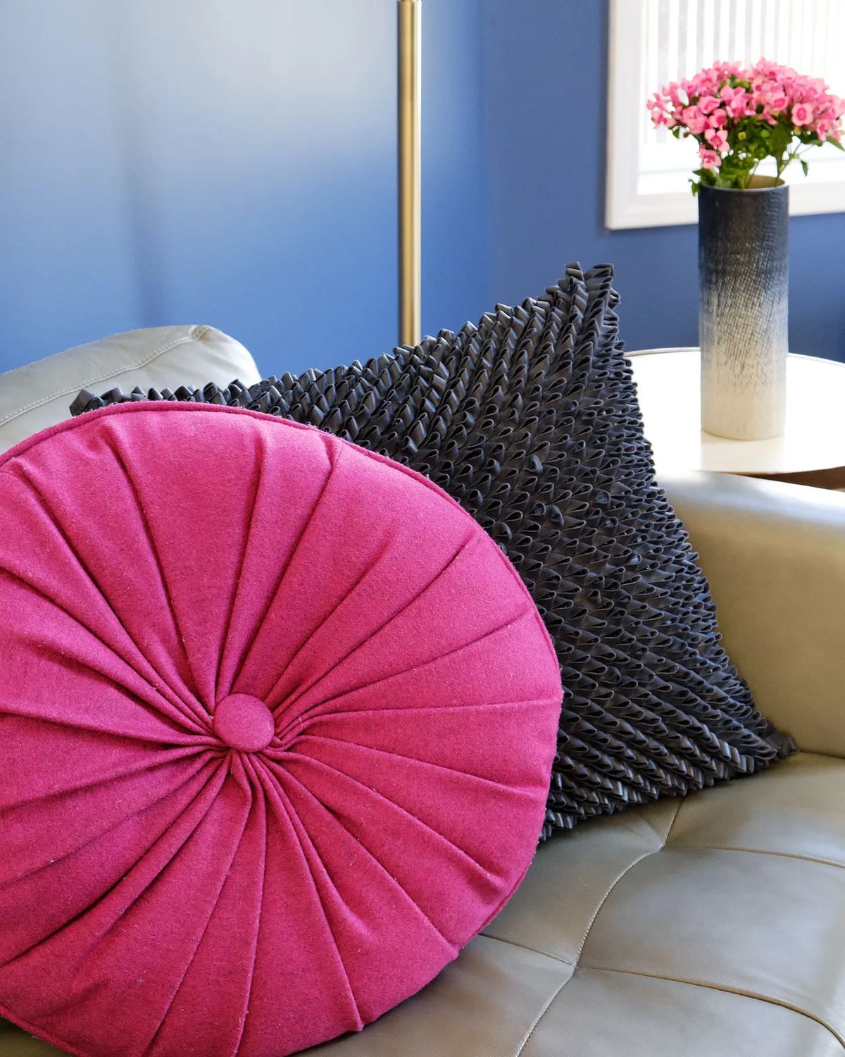 Living room with gray sofa, pink and black pillows, wooden side table, and blue walls with natural light