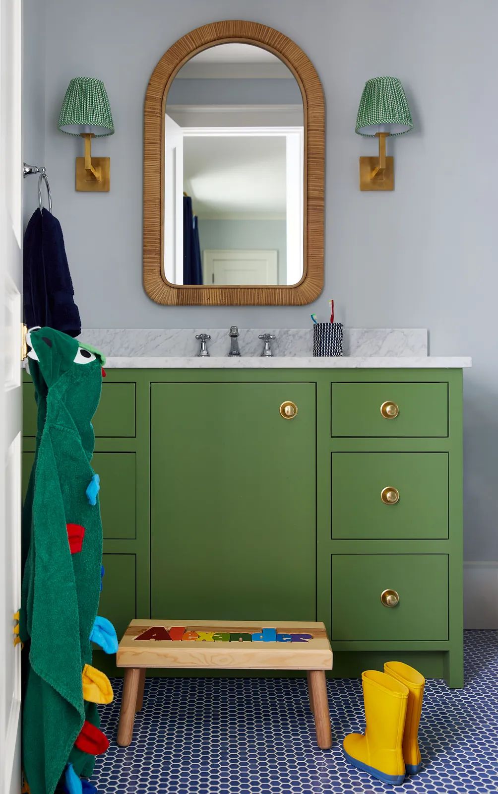 Bathroom with green vanity, marble countertop, rattan mirror, wall sconces, and blue patterned tile floor