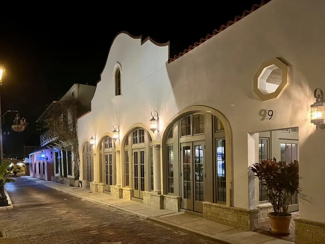 Exterior front view of a building with arched windows, tile roof, and ornamental wall sconces.