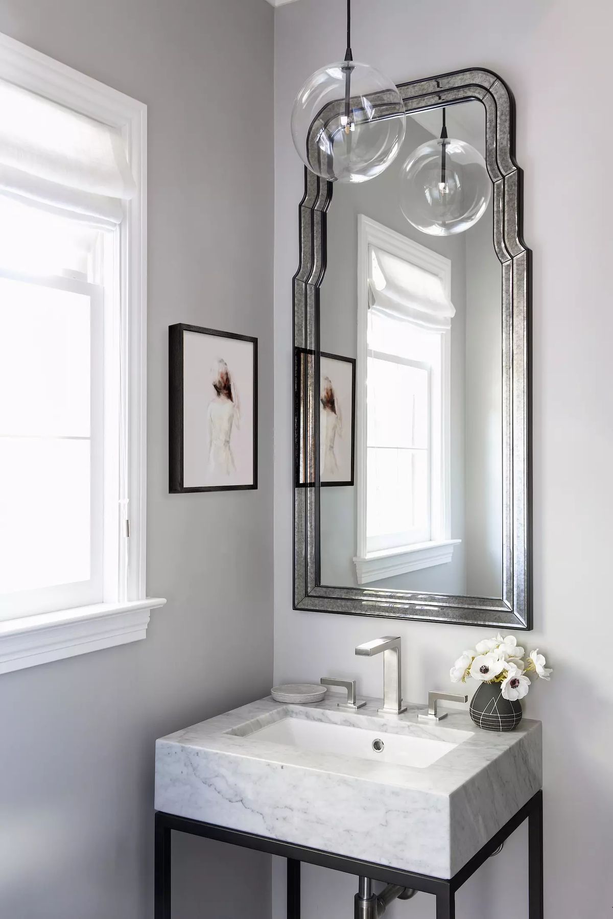 Bathroom with marble sink, ornate mirror, pendant lights, and a window with artwork on the wall.
