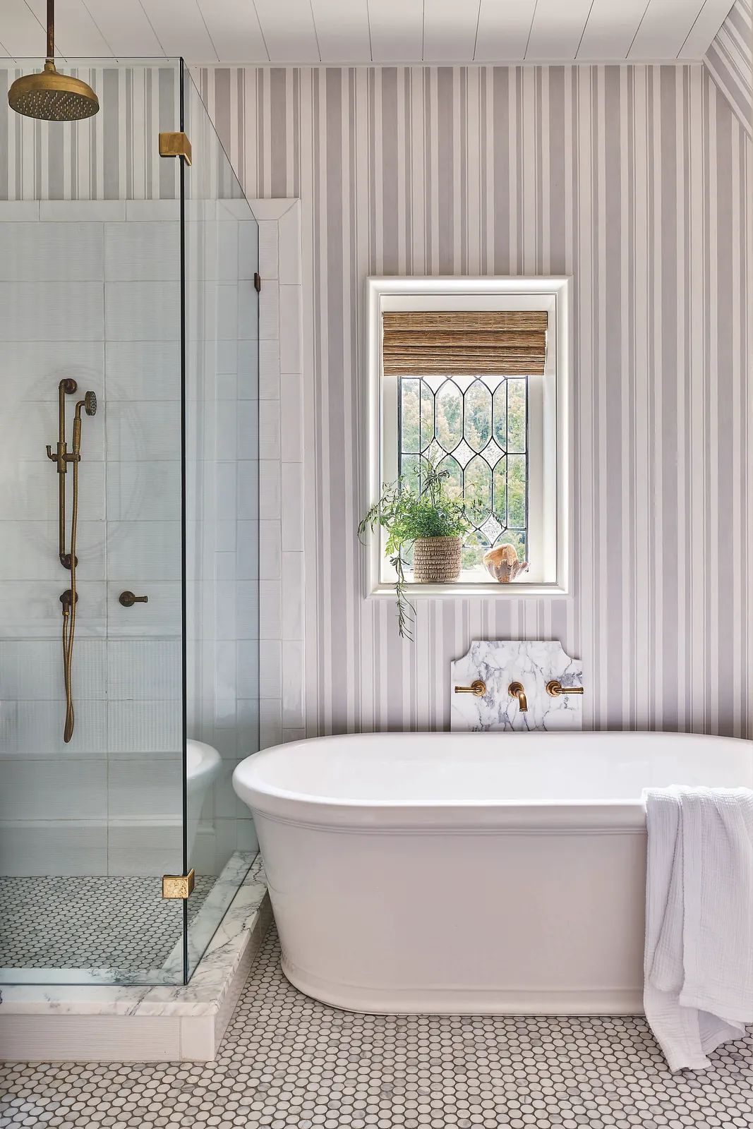 Bathroom with freestanding bathtub, glass shower, mosaic tile floor, and vertical striped wallpaper.