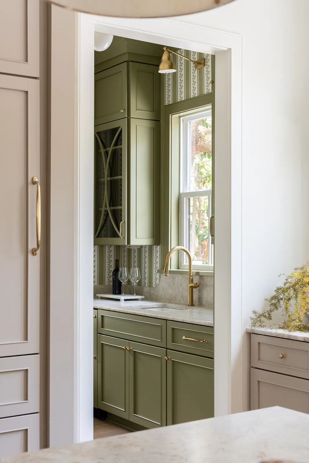 Kitchen with olive green cabinetry, marble countertop, window, and gold faucet.