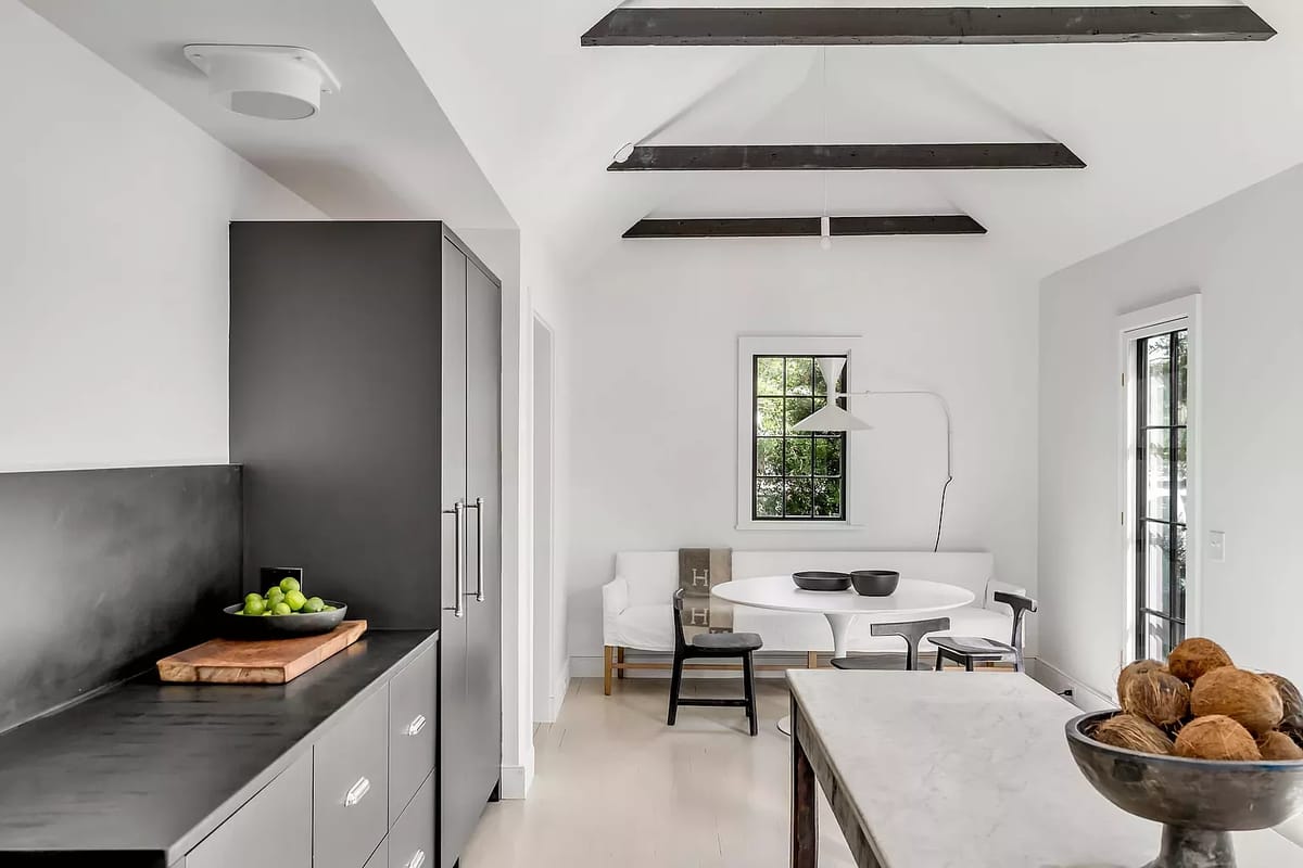Kitchen with dark cabinet, countertop, round table, chairs, bowl of decorative spheres, and exposed beams