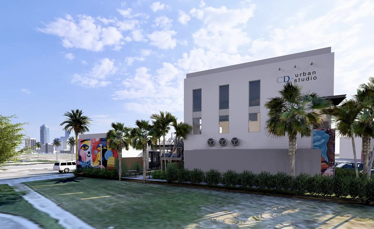Exterior front of a modern building with large windows, palm trees, murals, and landscaped entrance.