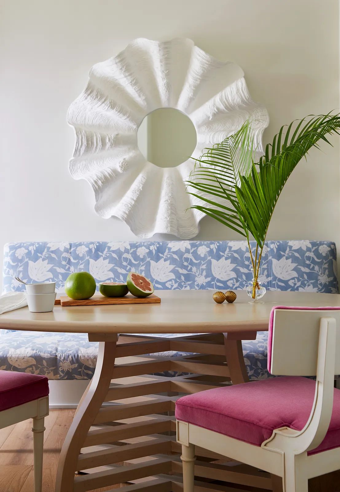 Dining room with table, pink chairs, blue bench, large mirror, and decorative fruit arrangement.