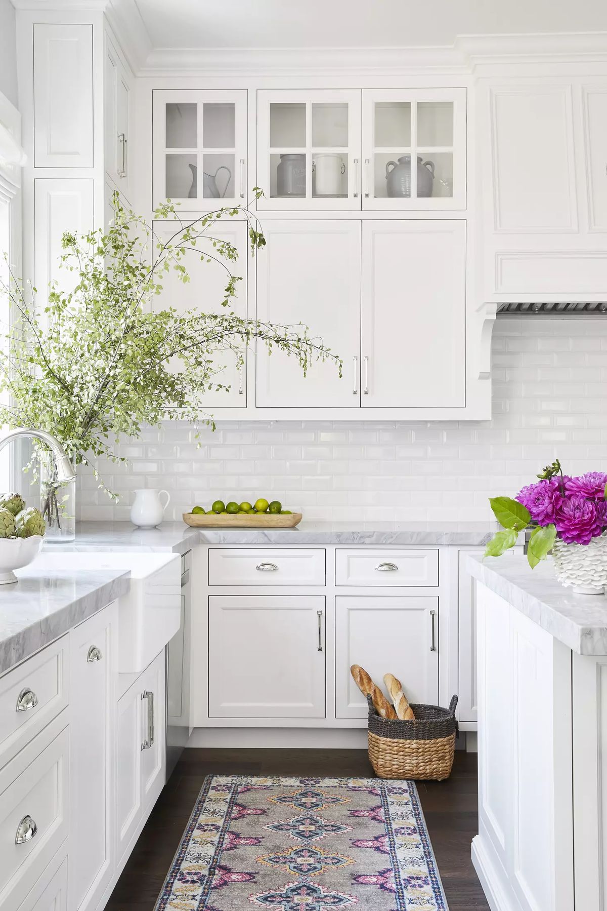 Kitchen with white cabinetry, marble countertop, limes, utensils basket, floral arrangement, and natural light.