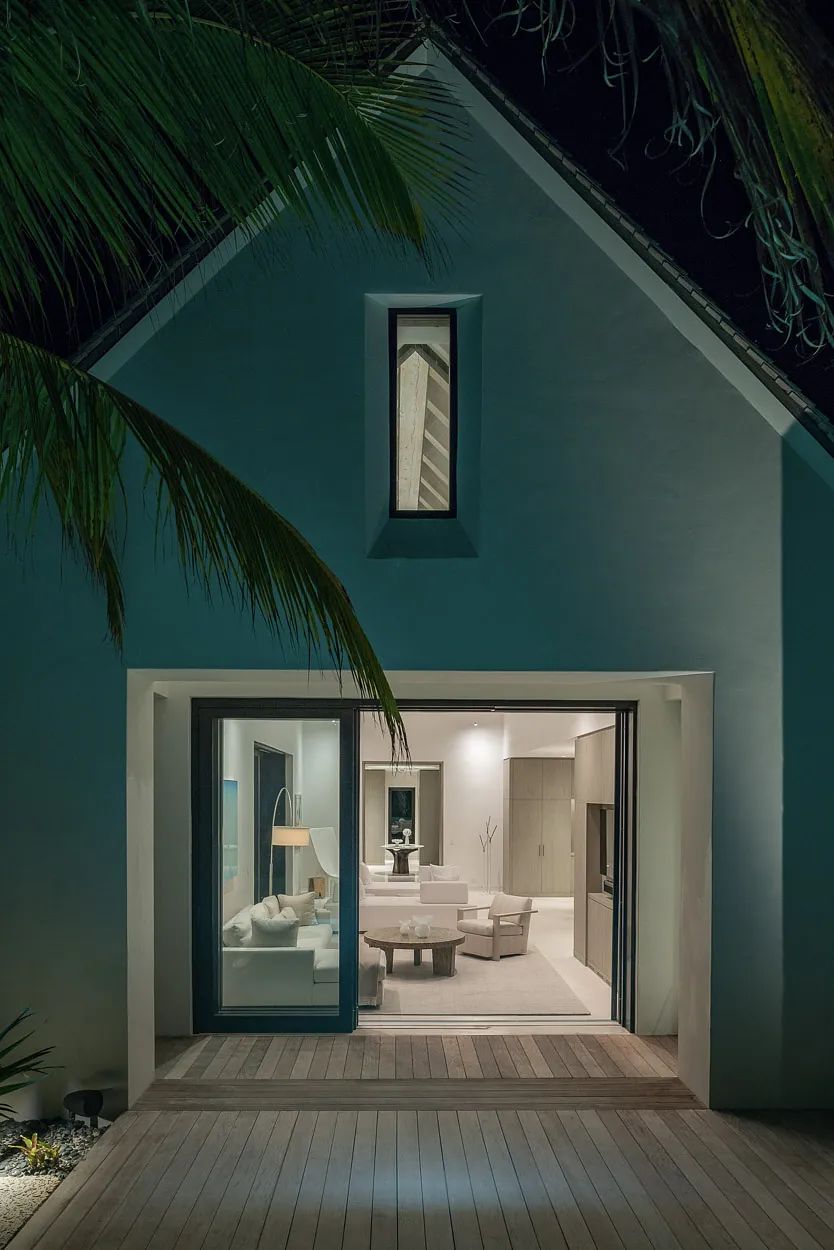 Living room view from outside with white sofas, coffee table, and large sliding glass door.