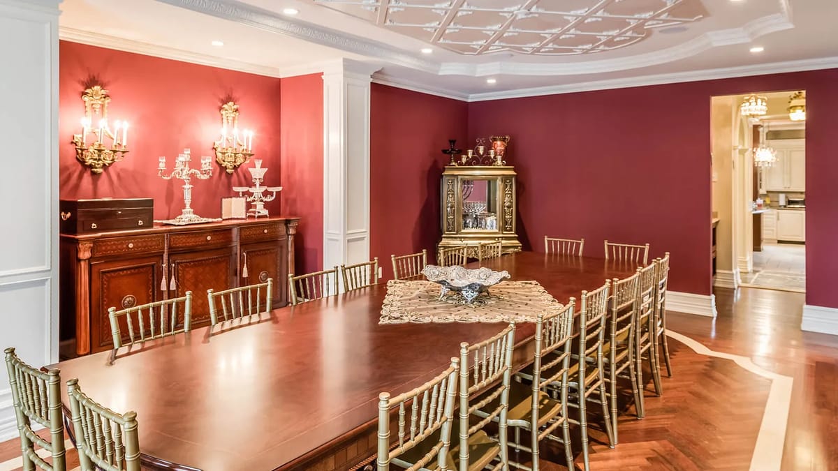 Dining room with large wooden table, gold chairs, red walls, sideboard, cabinet, and wall sconces.