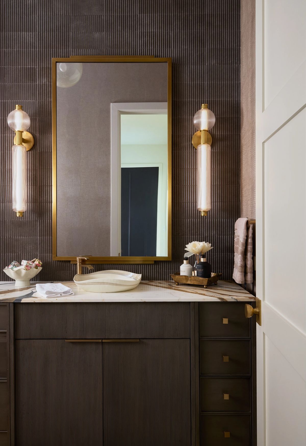 Bathroom with dark cabinet, white countertop, mirror, flower vase, and wall-mounted light fixtures.