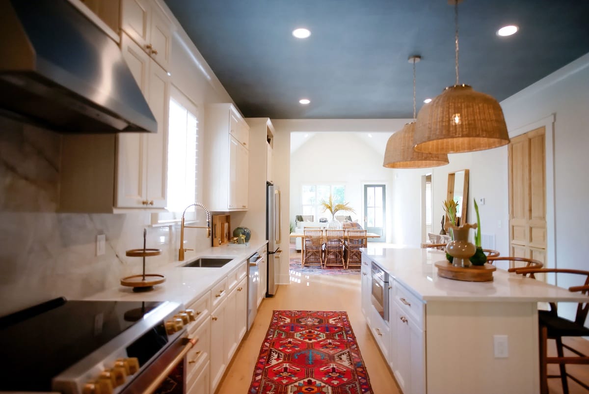 Kitchen with white cabinetry, marble countertop, black stove, stainless steel appliances, and patterned area rug.
