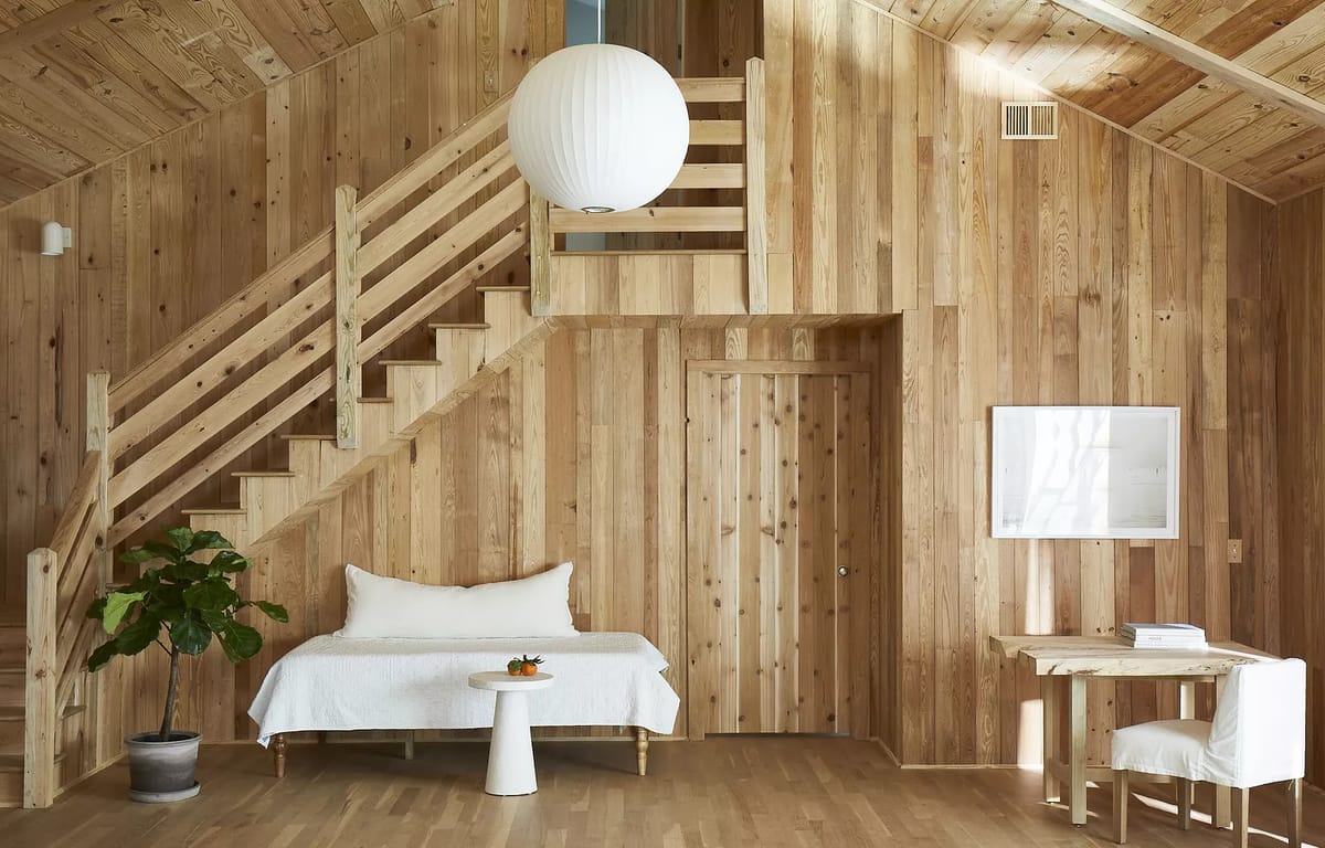 Living room with wood paneling, white daybed, round table, plant, stairs, and a paper lantern light fixture.