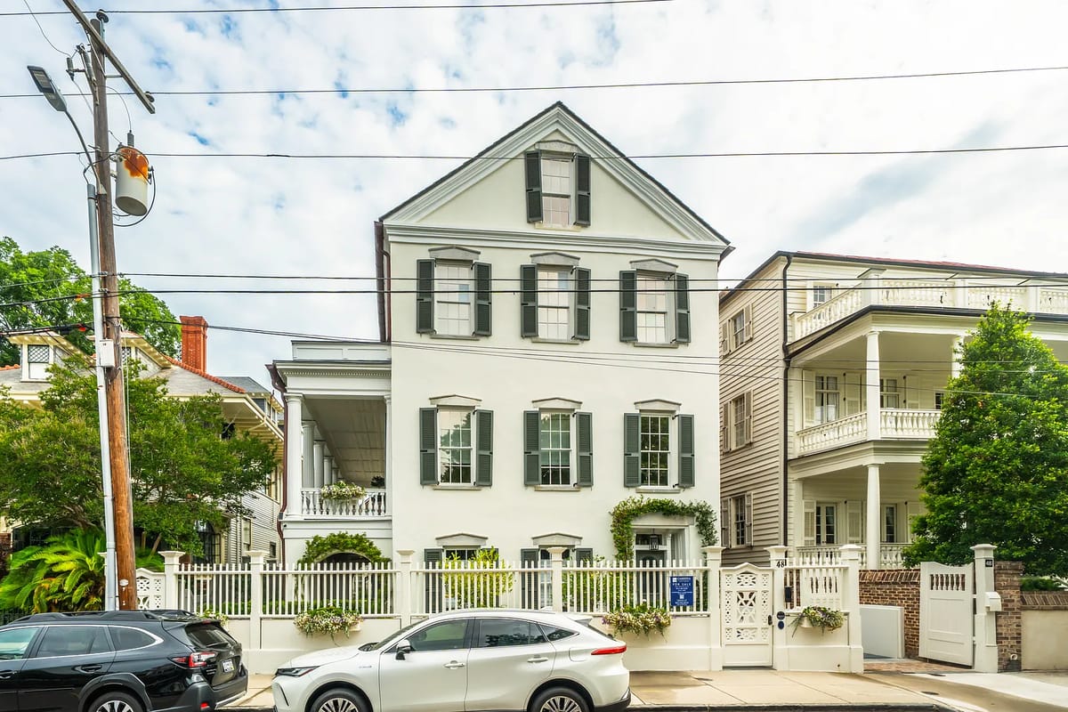 Front exterior view of a two-story white house with black shutters and a porch.