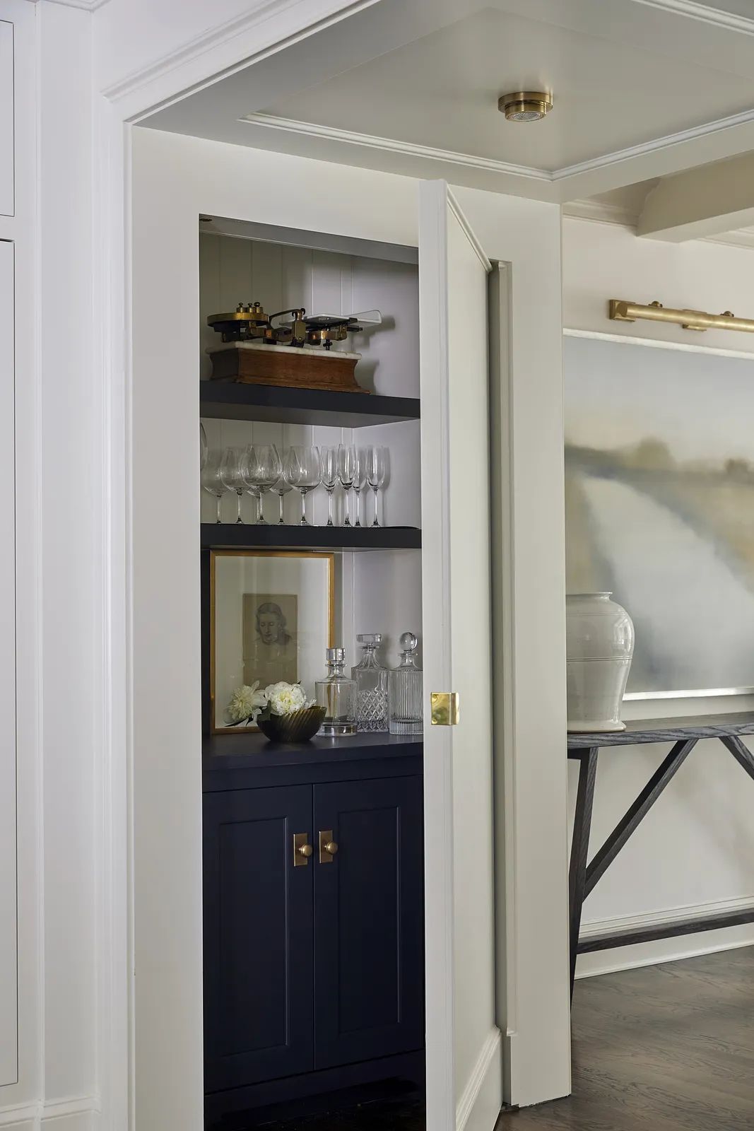 Small bar area with dark blue cabinet, glassware, decorative items, and adjacent wall painting.
